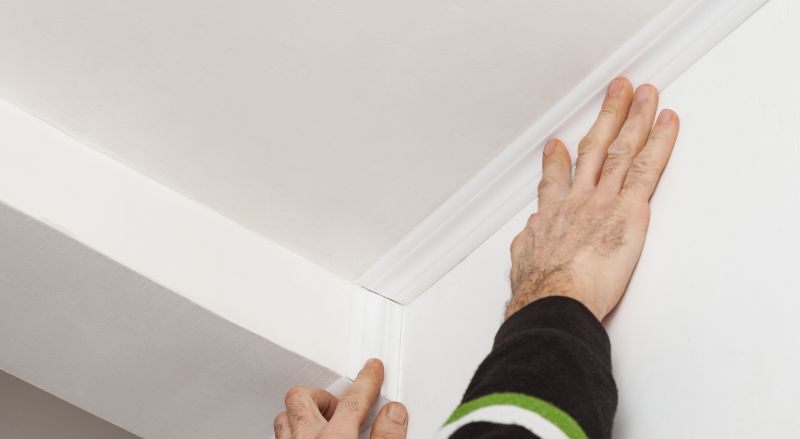 homme en train de coller une moulure fine et plate dans un angle de plafond