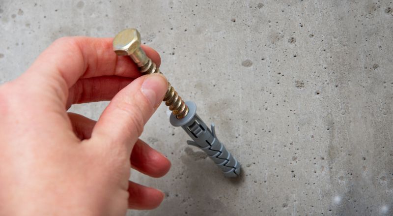 une main tient une vis grise sur le fond d un mur de beton gris en gros plan
