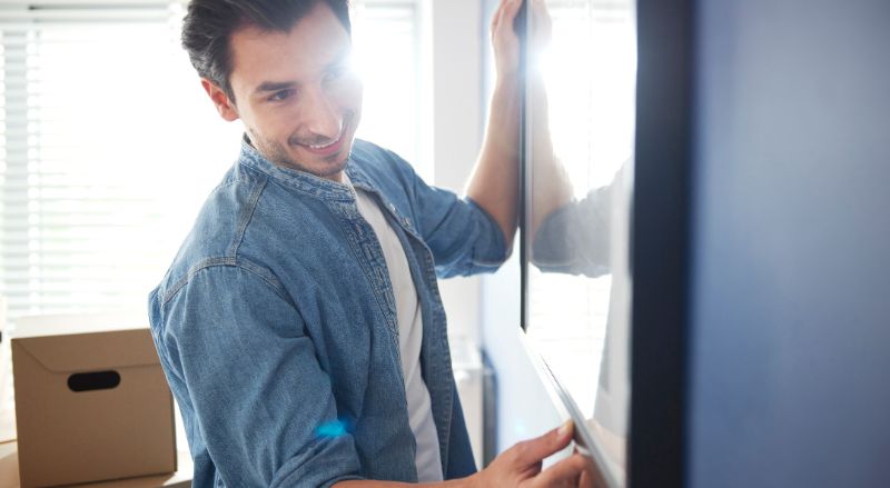 un jeune homme en train d accrocher un tableau sur un mur peint